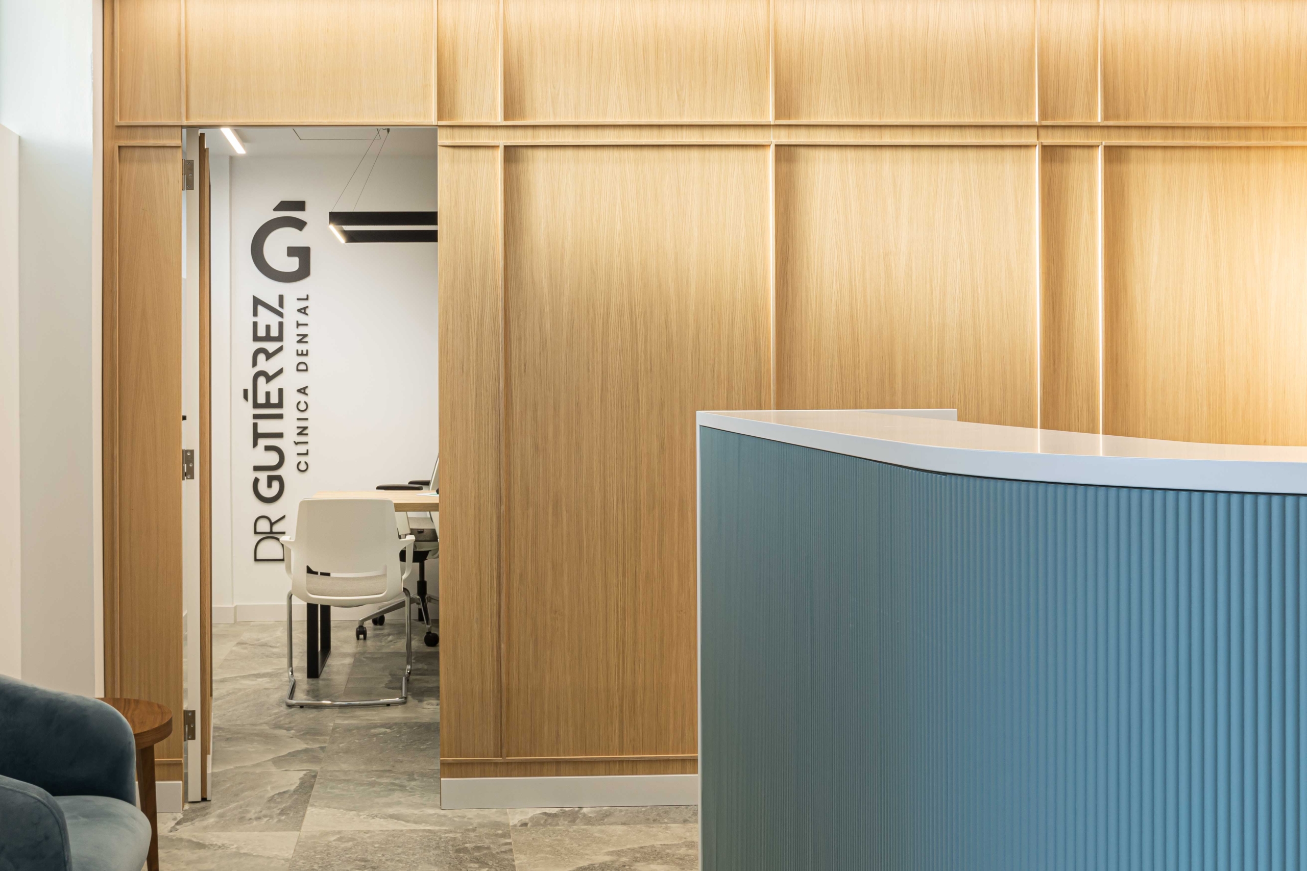 Sala de recepción y sala de reuniones con acabado en madera y con ordenador y diseño logo con nombre ¨Dr Gutierrez¨
