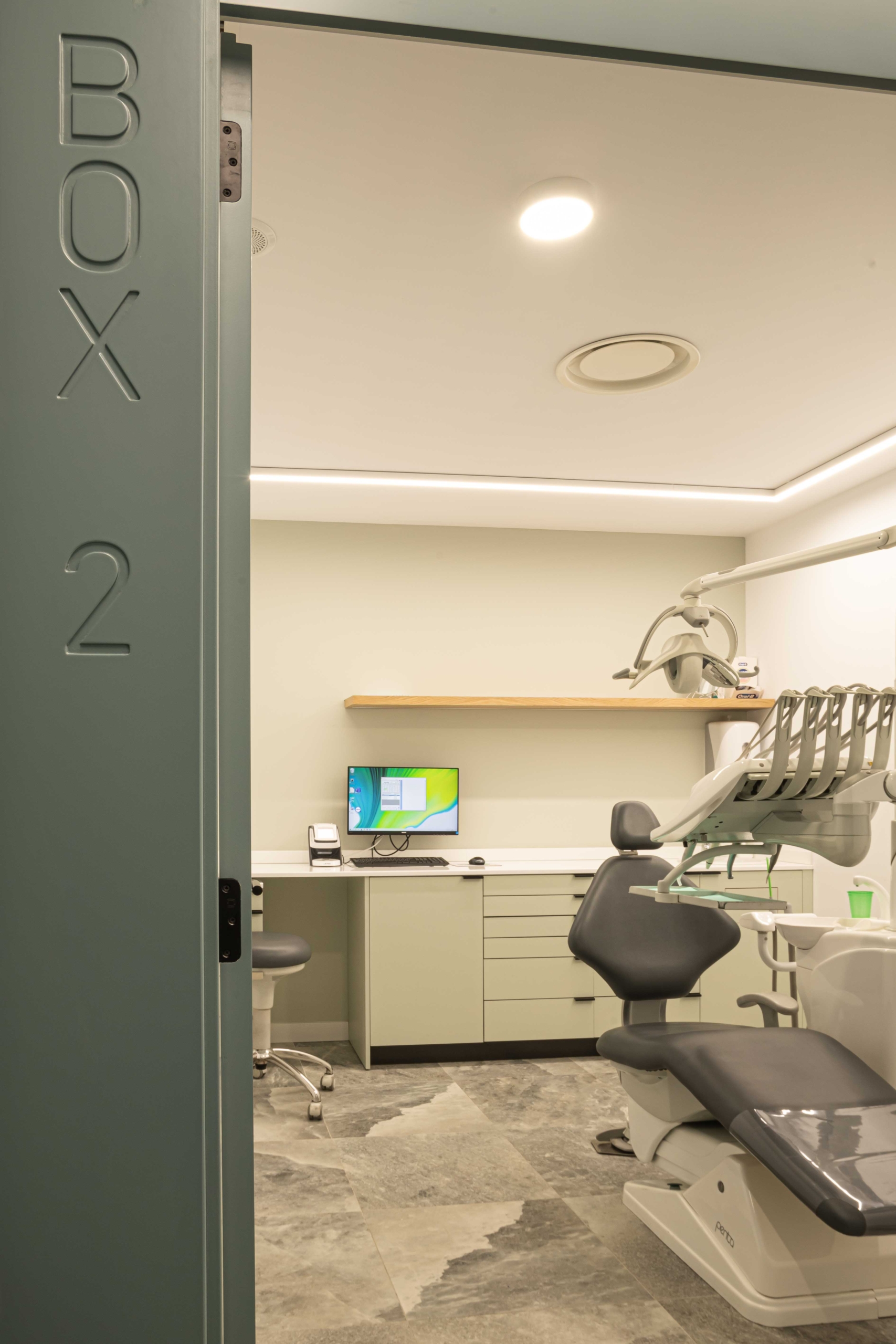 Puerta con nombre ¨Box 2¨con mobiliario protesico y silla oncolagica en acabado en gris, con ordenador