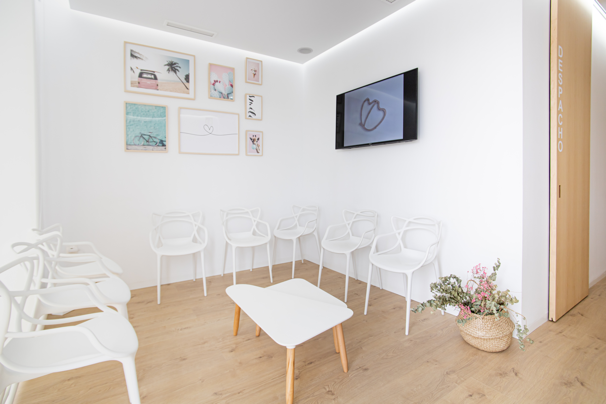 Sala de consulta con sillas con pantalla en la pared y acabado moderno en madera y en blanco