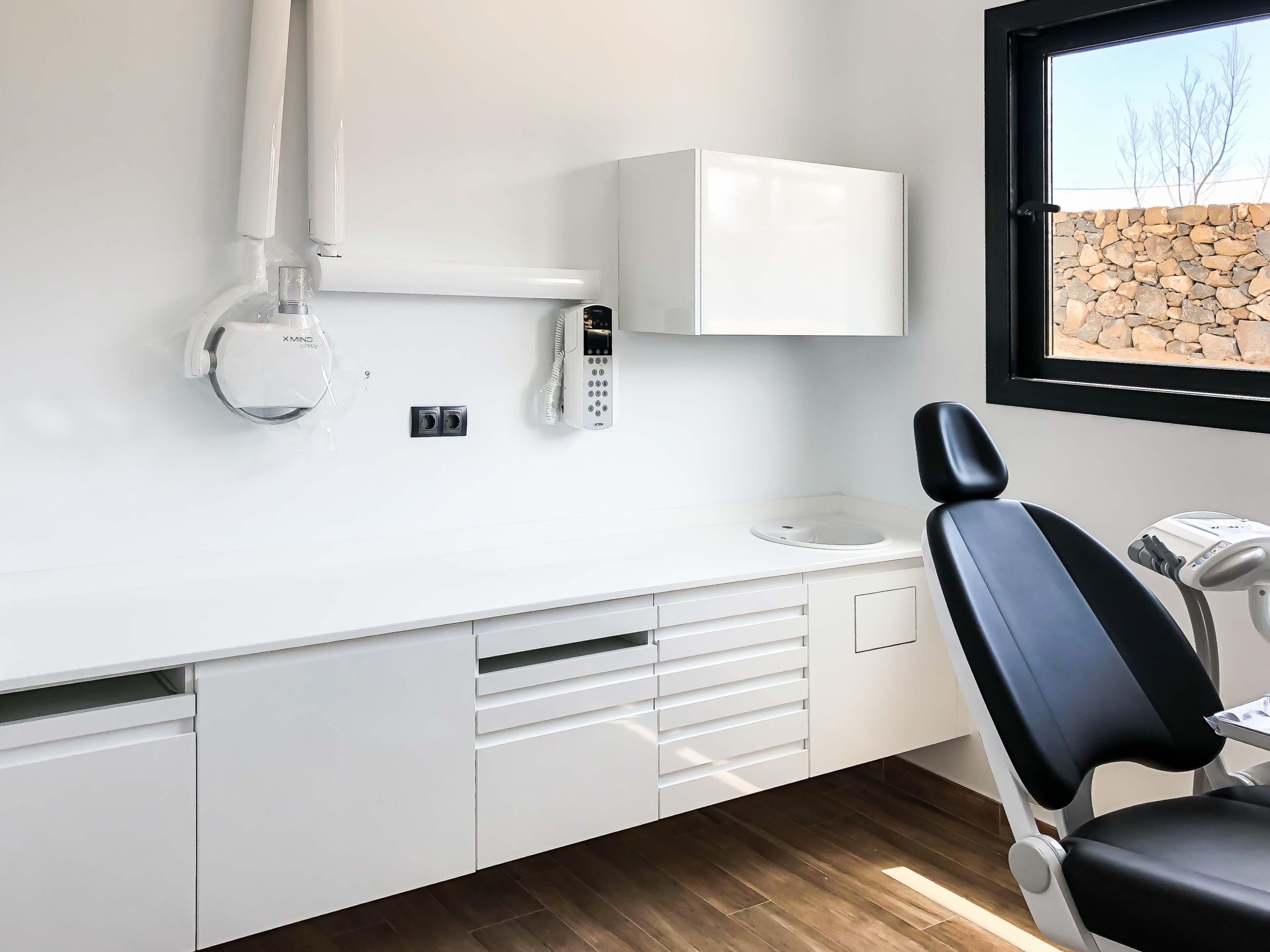 Mobiliario protesico con encimera de color blanca, mueble dispensador,  con ventana al exterior y silla odontologica